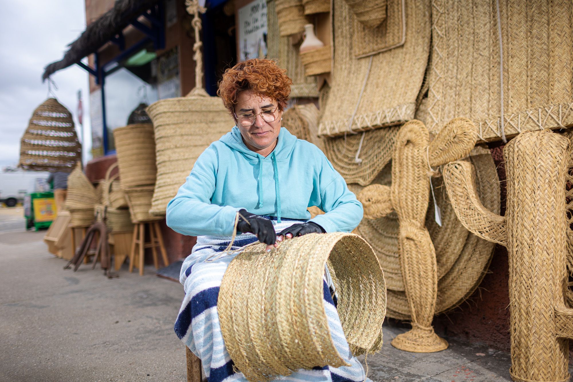 Caridad Sumariva, de Sanlúcar, una de las pocas esparteras de Andalucía, cosiendo una persiana frente a su tienda.