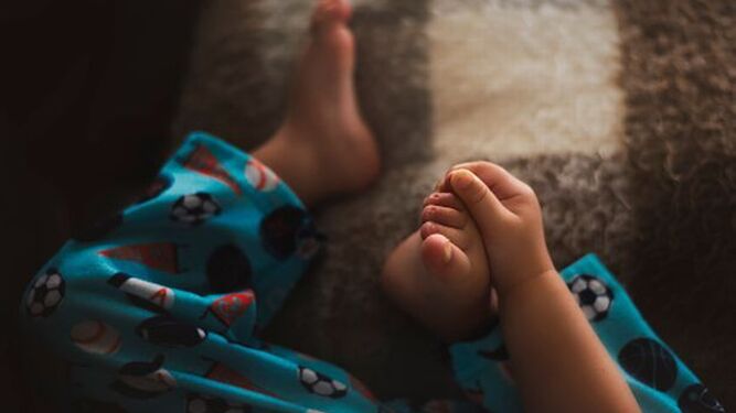 Niño se toca los pies en una foto de archivo. 
