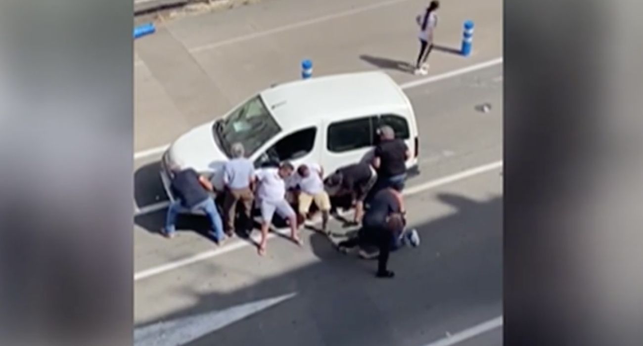 Momento en el que varias personas levantan a pulso una furgoneta para rescatar a una joven que había quedado atrapada abajo tras ser atropellada.