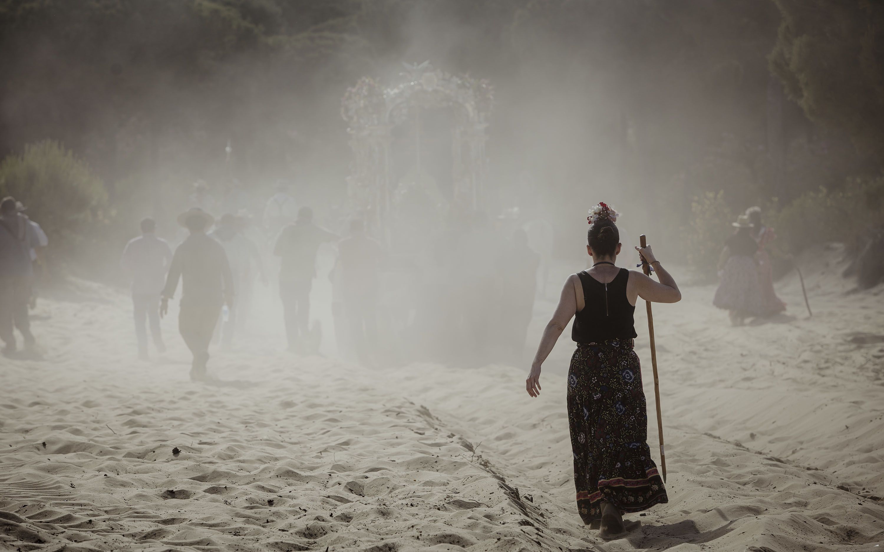 Una peregrina camina sola entre una nuebe de polvo tras la carreta de plata.