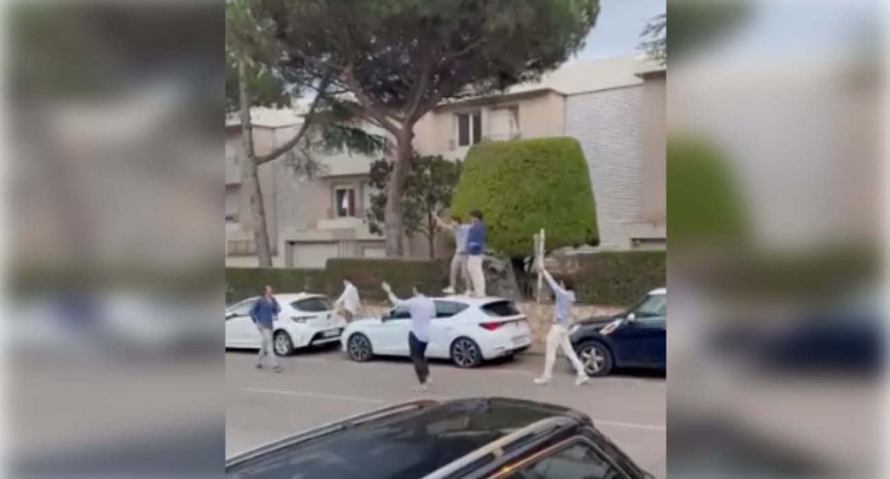 Seis jóvenes, con una señal de tráfico y subidos a lo alto de un coche. 