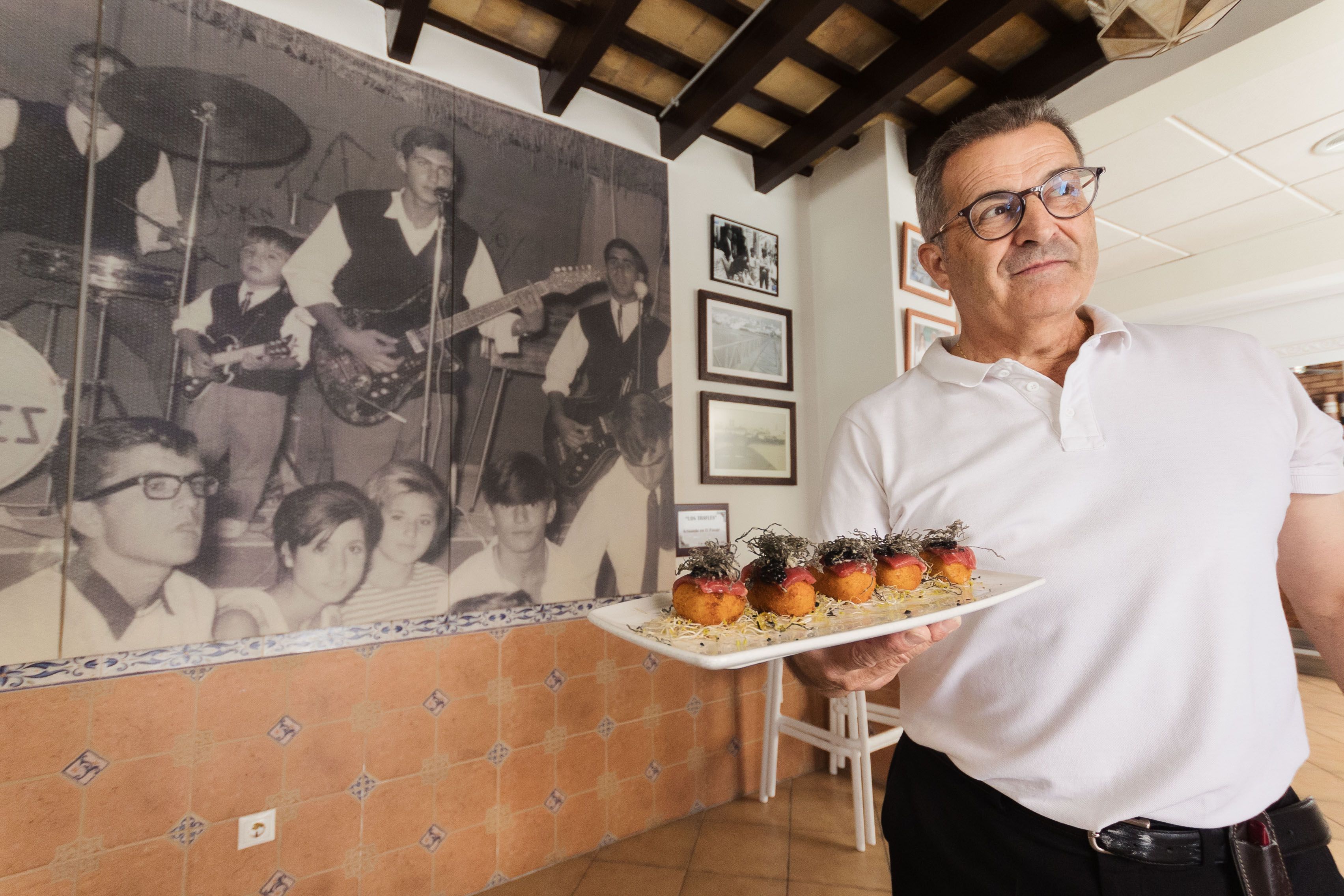 Jesús Rubio, encargado de El Pasaje en Conil, con uno de los platos y delante de una foto gigante de la época en la que actuaban los Trafles en el local.