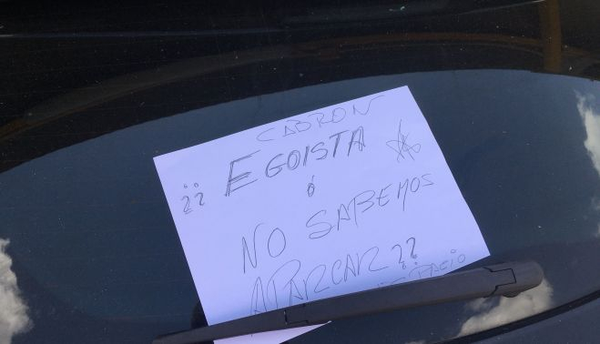 El cartel colocado en el parabrisas del coche aparcado en dos plazas.