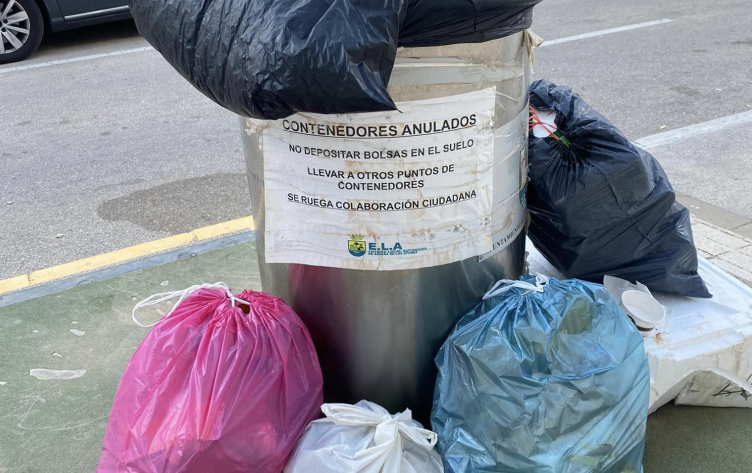 Un contenedor averiado rodeado de bolsas de basura. 