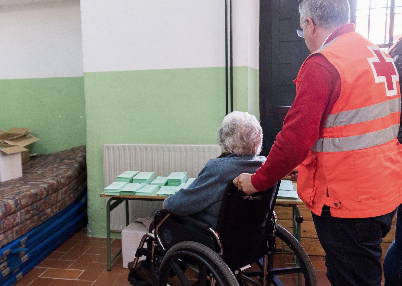 Un voluntario de Cruz Roja ayudando a una persona mayor a votar.