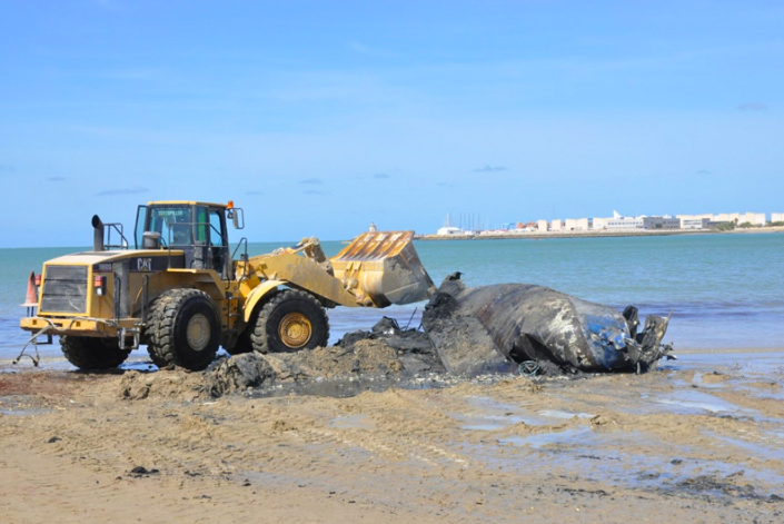 Una excavadora de gran tonelaje troceando el velero y retirándolo progresivamente de la arena. 