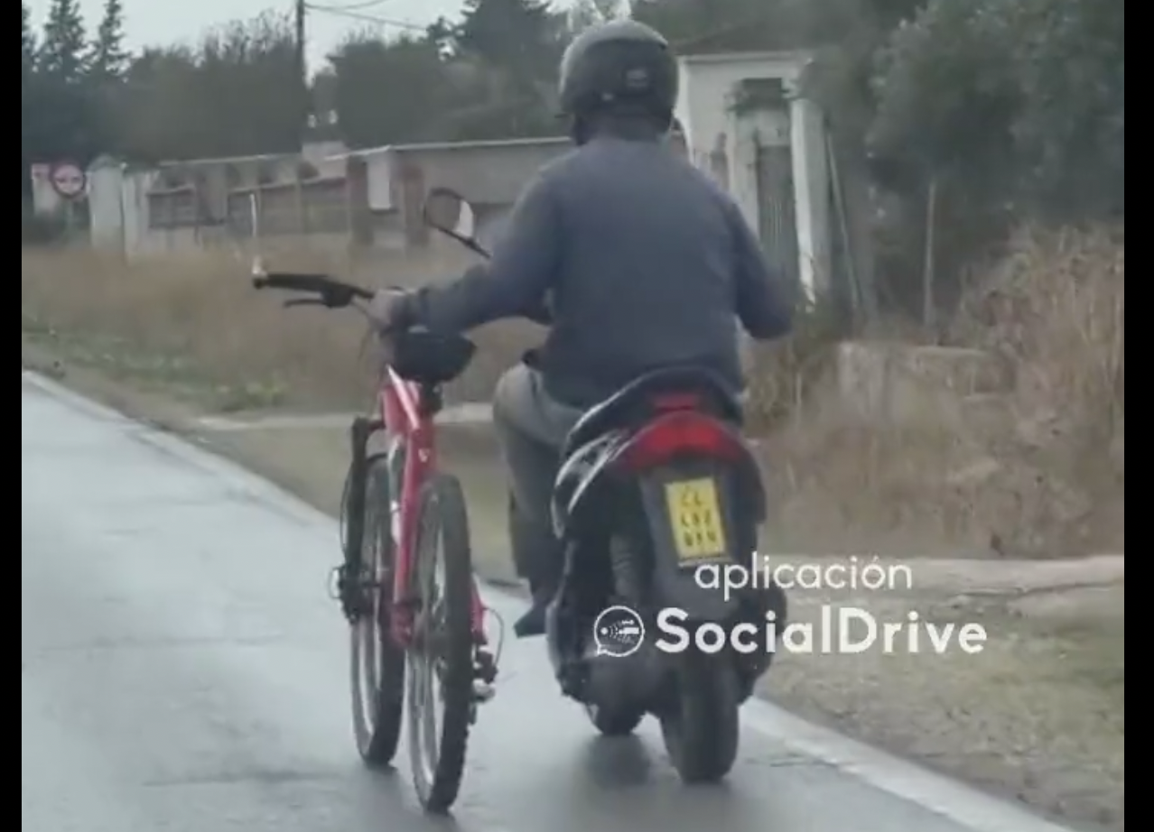 Un hombre circula con su moto mientras sujeta una bicicleta en Chiclana.