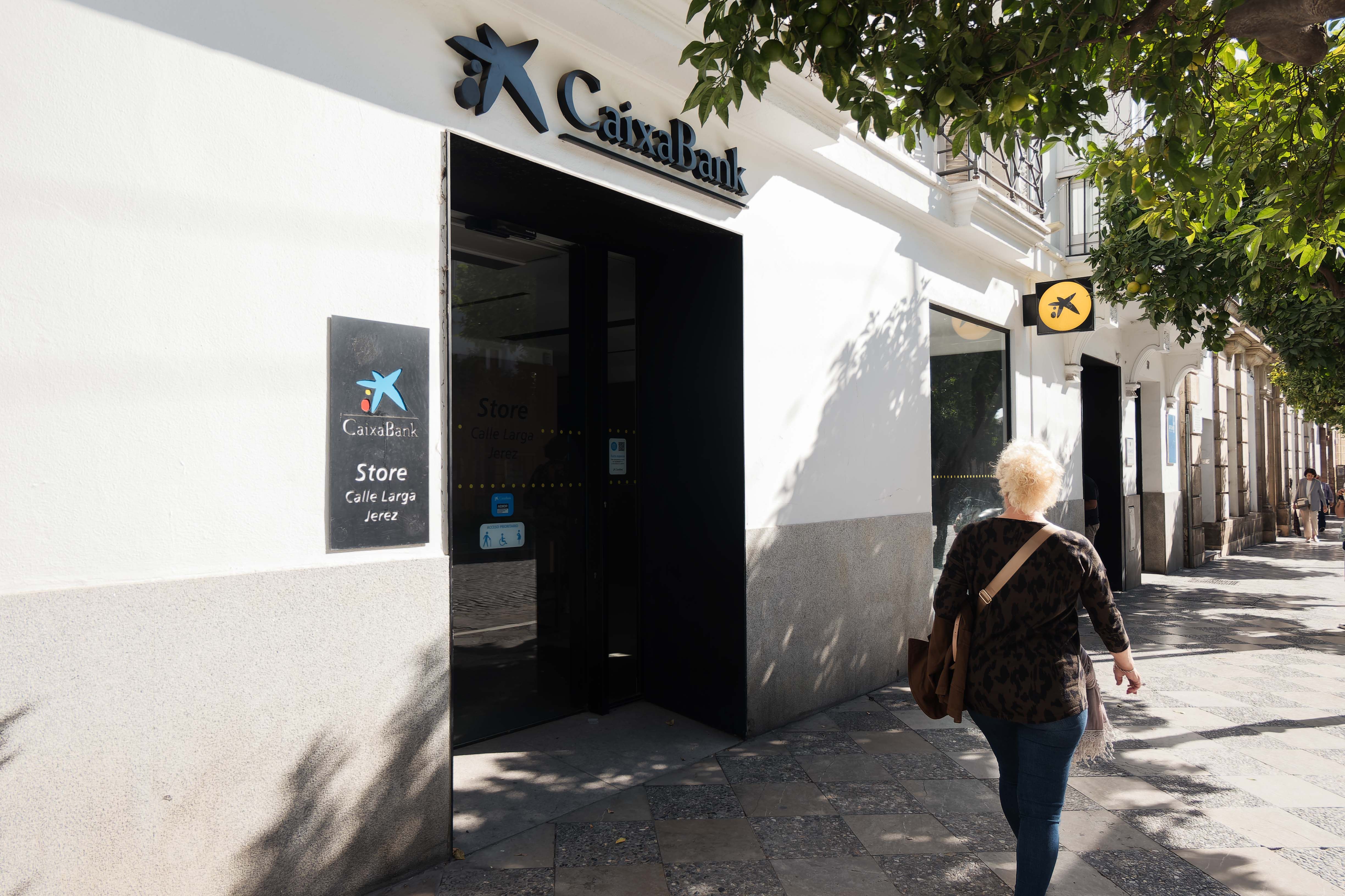 Una mujer pasea por delante de una oficina de CaixaBank, una de las entidades con más hipotecados en España.