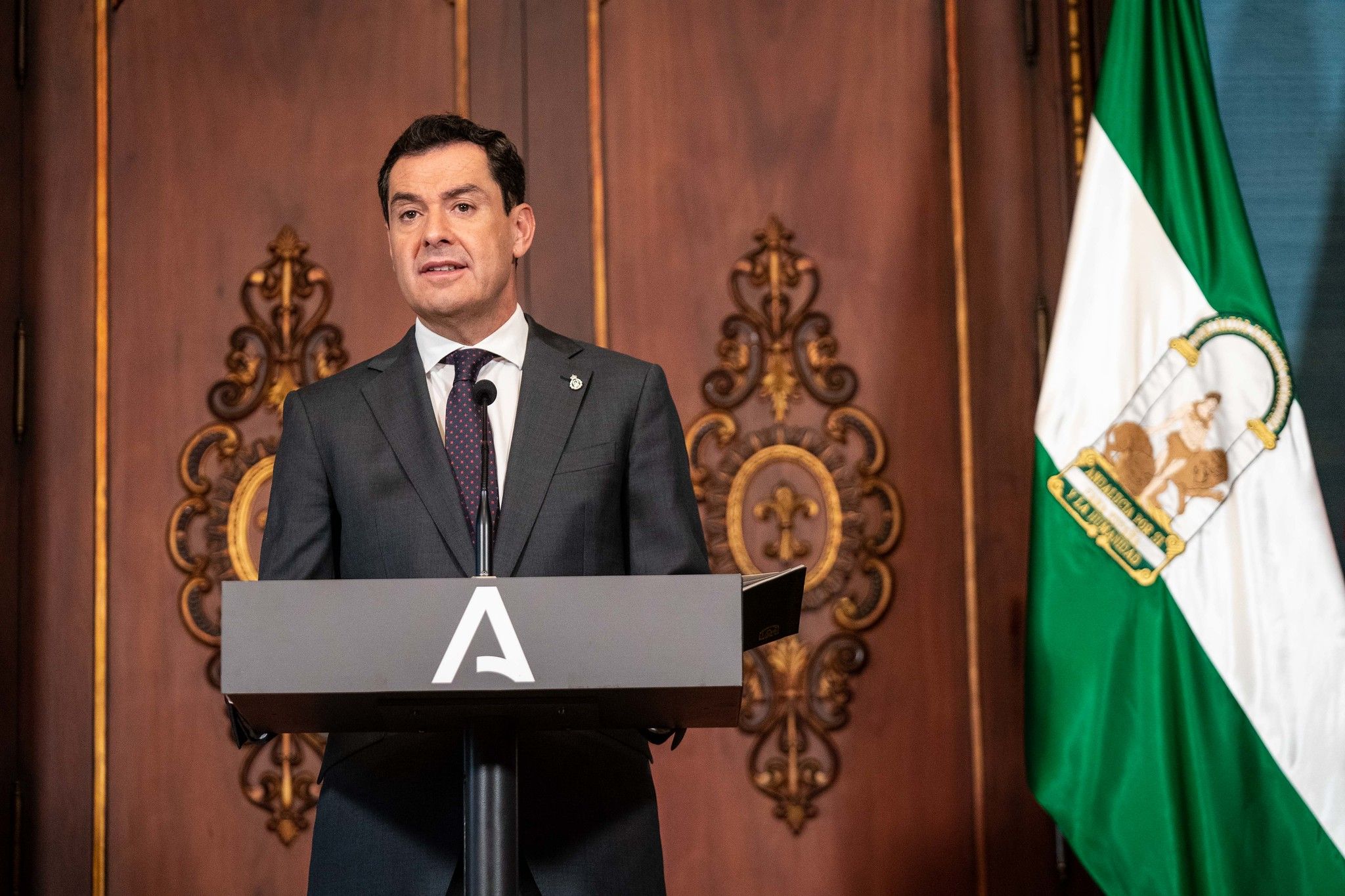 El presidente andaluz, Juan Manuel Moreno, con la bandera de Andalucía al lado.