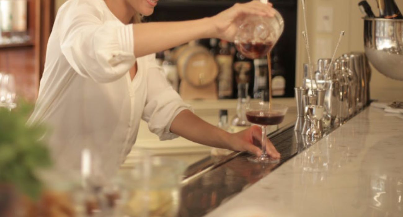 Una camarera sirve una copa en un bar a un cliente. 