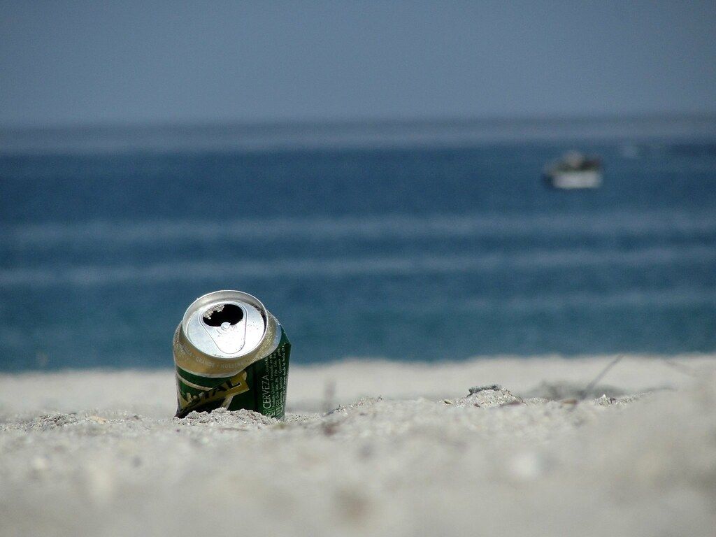 Una lata de cerveza semienterrada en la playa 