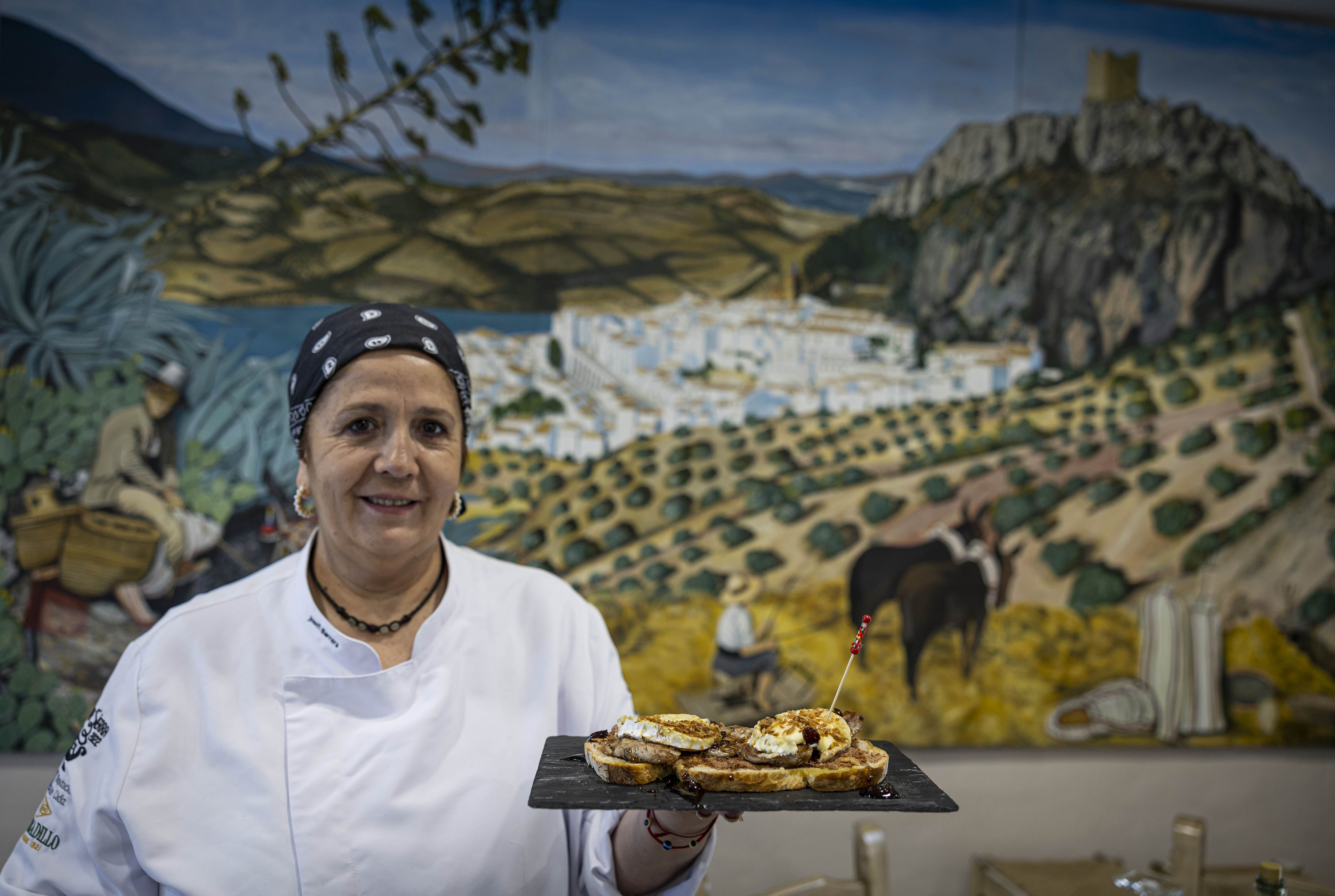 Josefi Barrera, con su paté casero, plato estrella en el restaurante La Era. Al fondo, una imagen pictórica de Zahara de la Sierra.