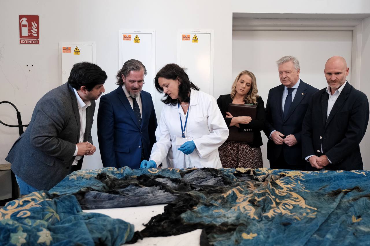 El viceconsejero en el IAPH atendiendo las indicaciones de una técnico sobre un manto dañado por el fuego.