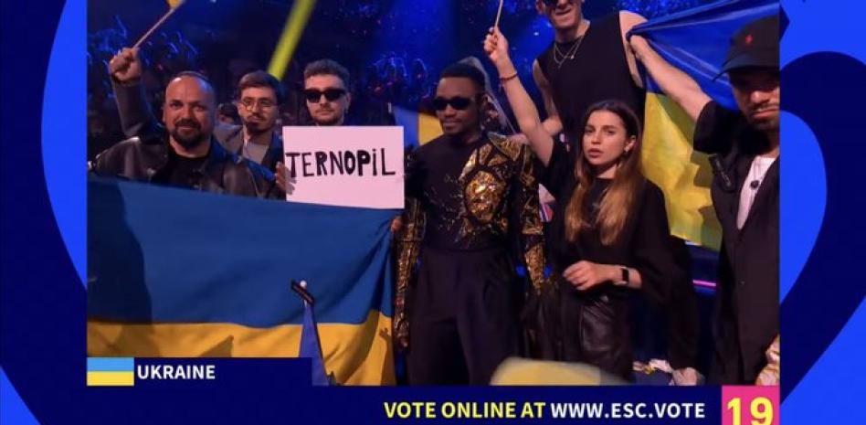 Los representantes de Ucrania en Eurovisión con el cartel de la ciudad bombardeada.