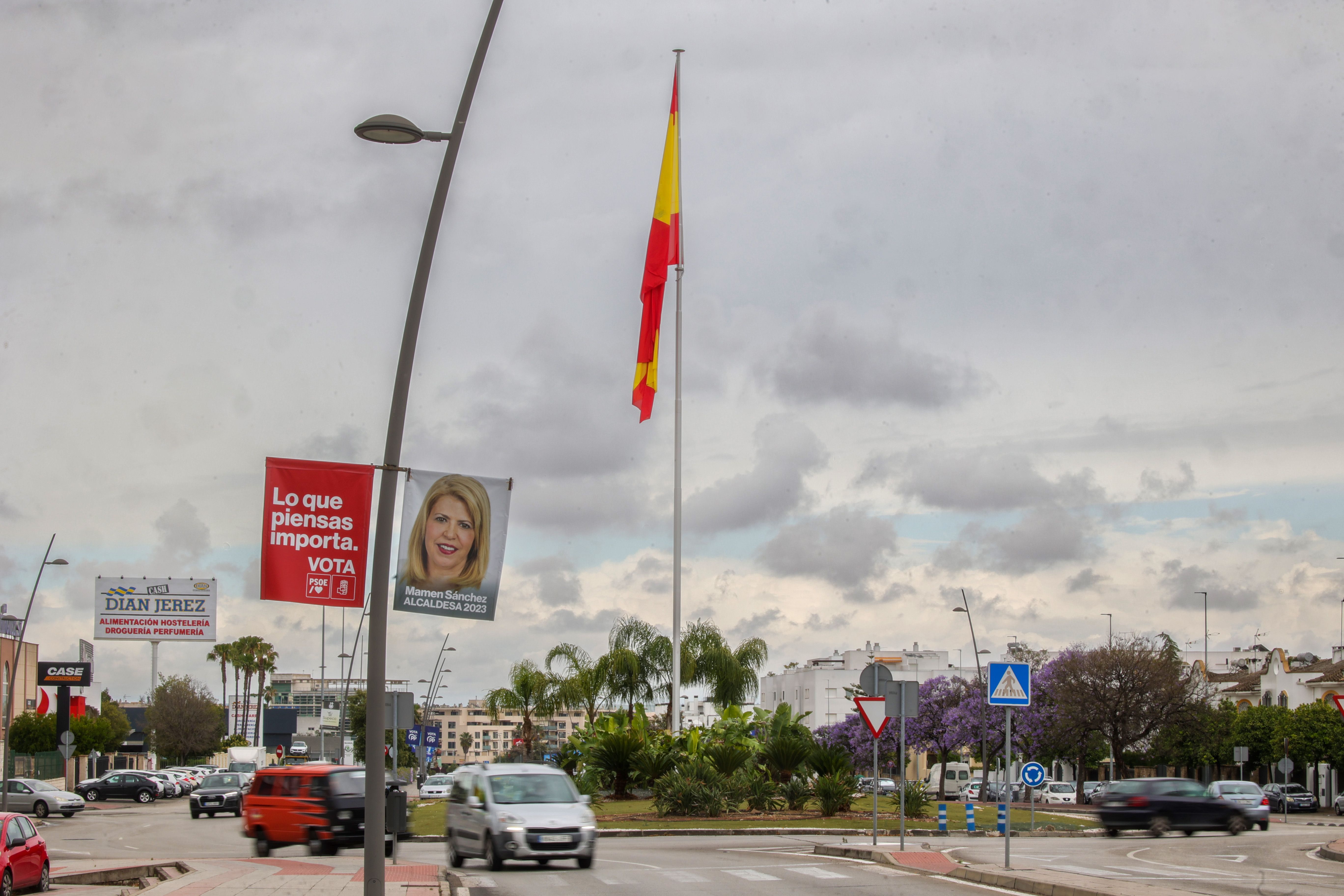 Bandera de España en la avenida Adolfo Suárez, en Jerez, con propaganda electoral del PSOE de Mamen Sánchez en primer término.