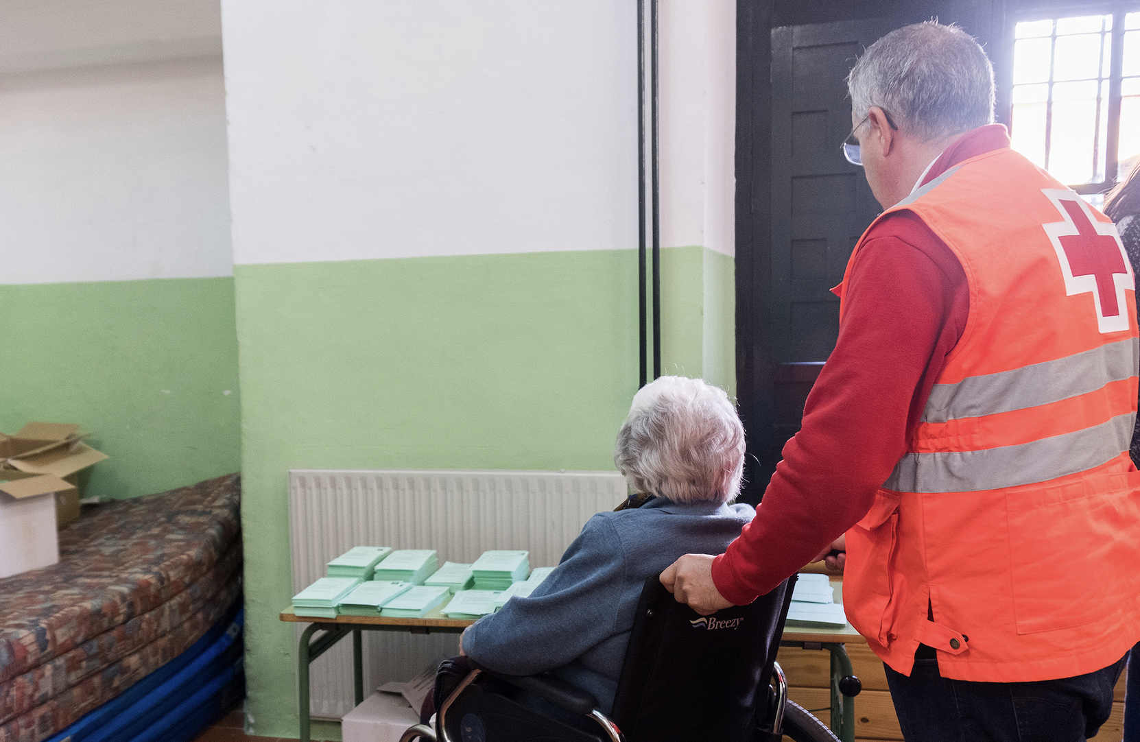 Un voluntario de la Cruz Roja acompañando a un a persona mayor a votar en unas pasadas elecciones. 