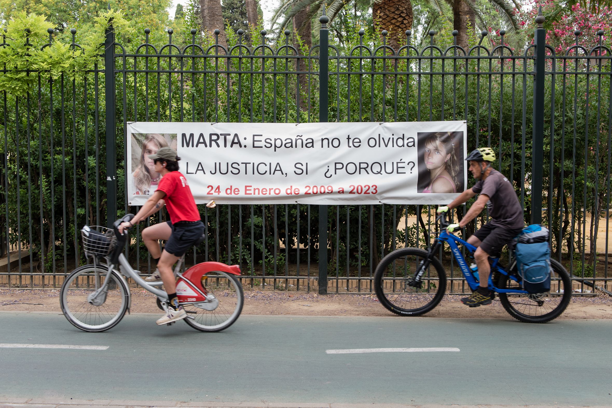 Dos ciclistas pasan frente a un cartel que recuerda a Marta del Castillo.