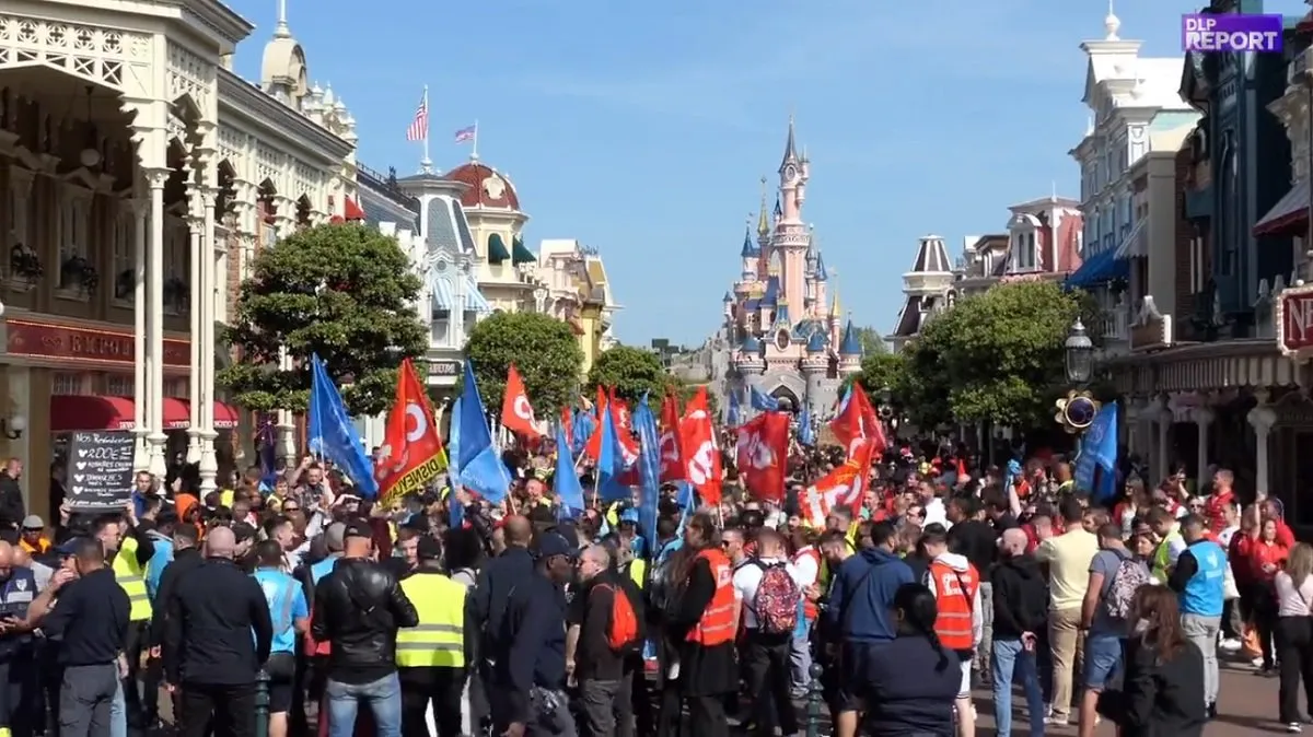 Manifestación de trabajadores en la avenida principal del parque con el emblemático castillo de Disneyland al fondo.