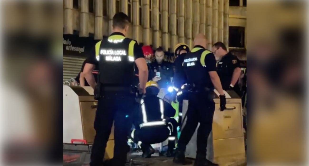 Bomberos y agentes de la Policía Local de Málaga, intentando rescatar a un joven de un contenedor de basuras.
