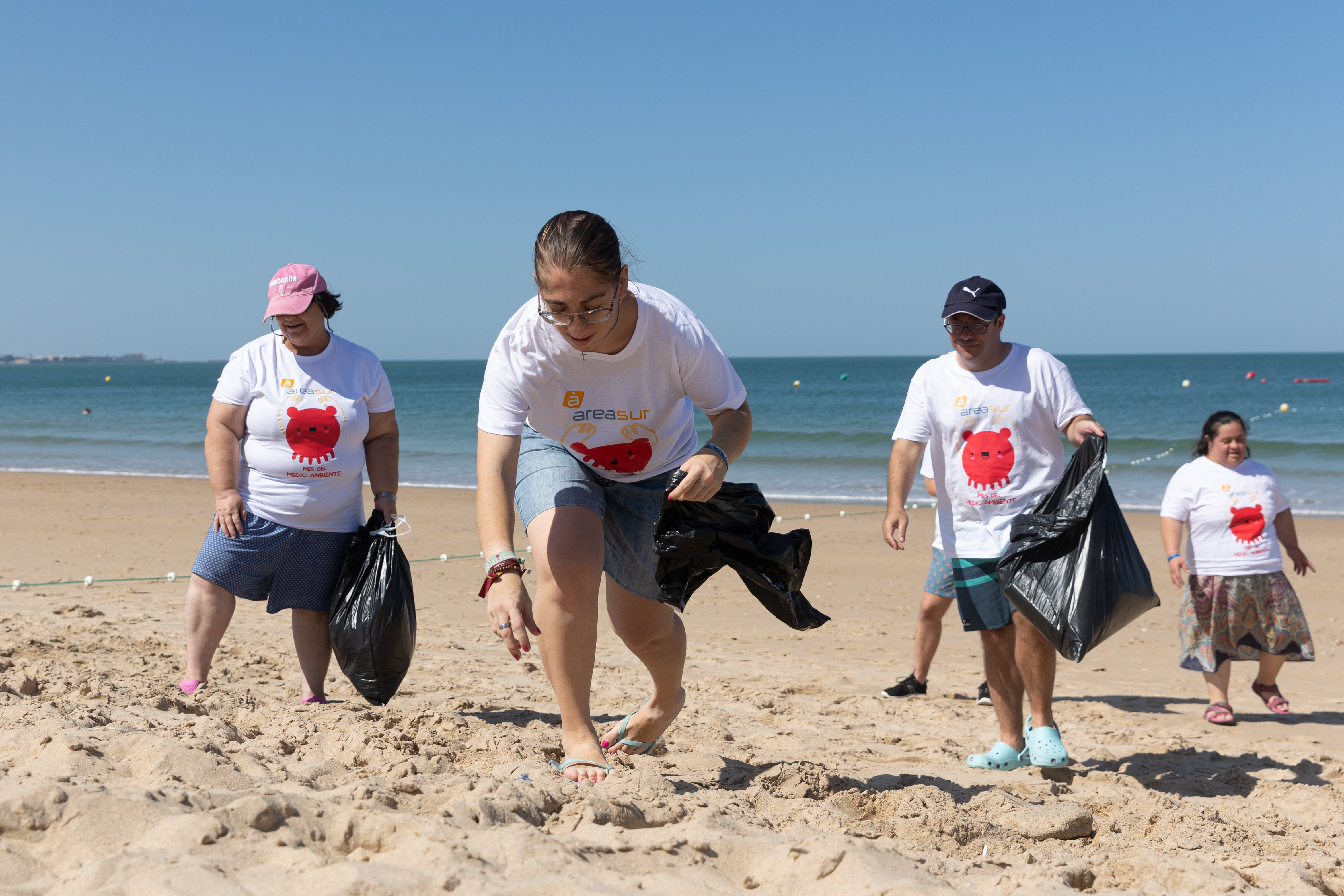 Voluntarios en plena labor de recogida de residuos en al arena de la playa. 