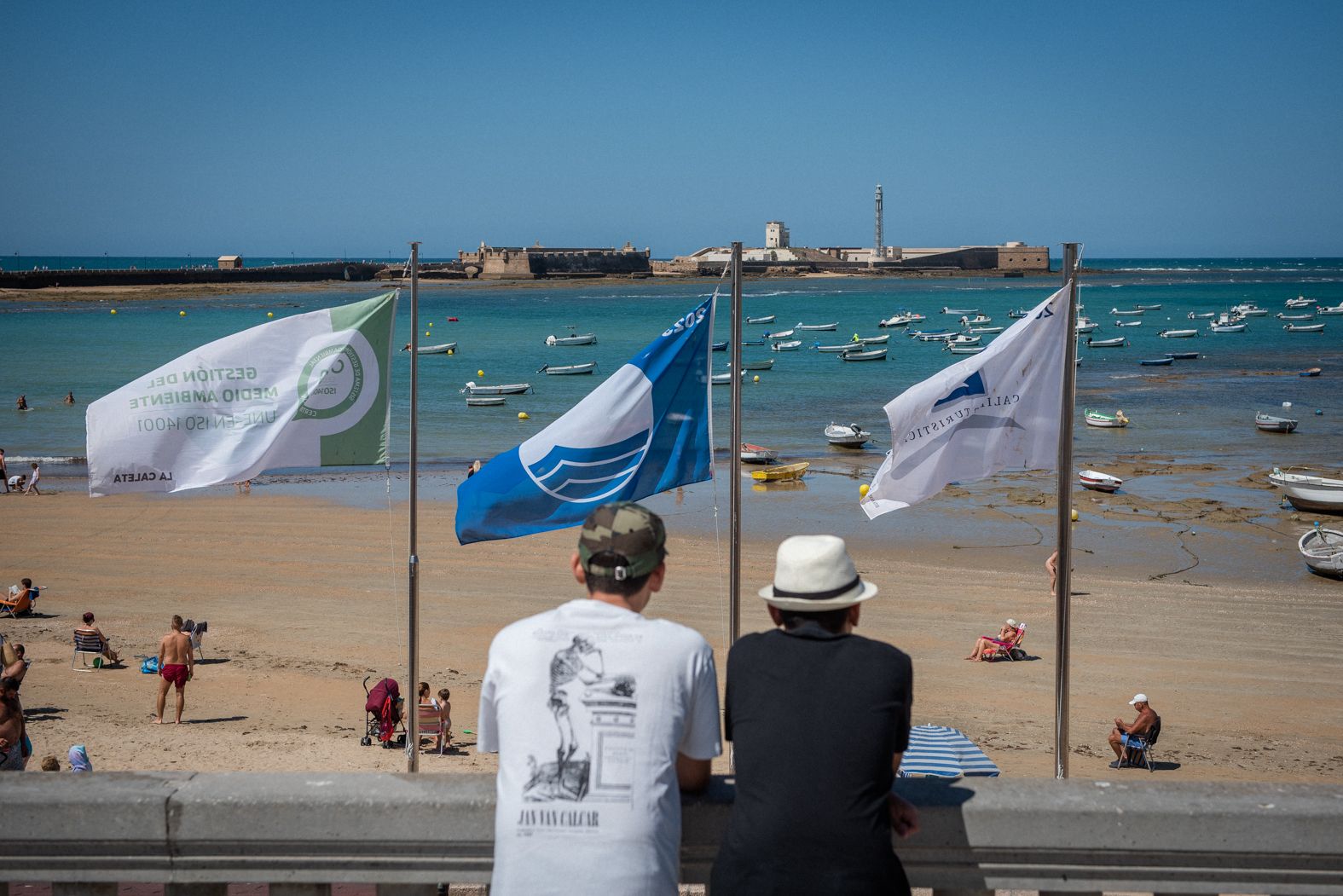 Dos personas observan el horizonte, con el castillo de San Sebastián al fondo, en la playa de La Caleta.