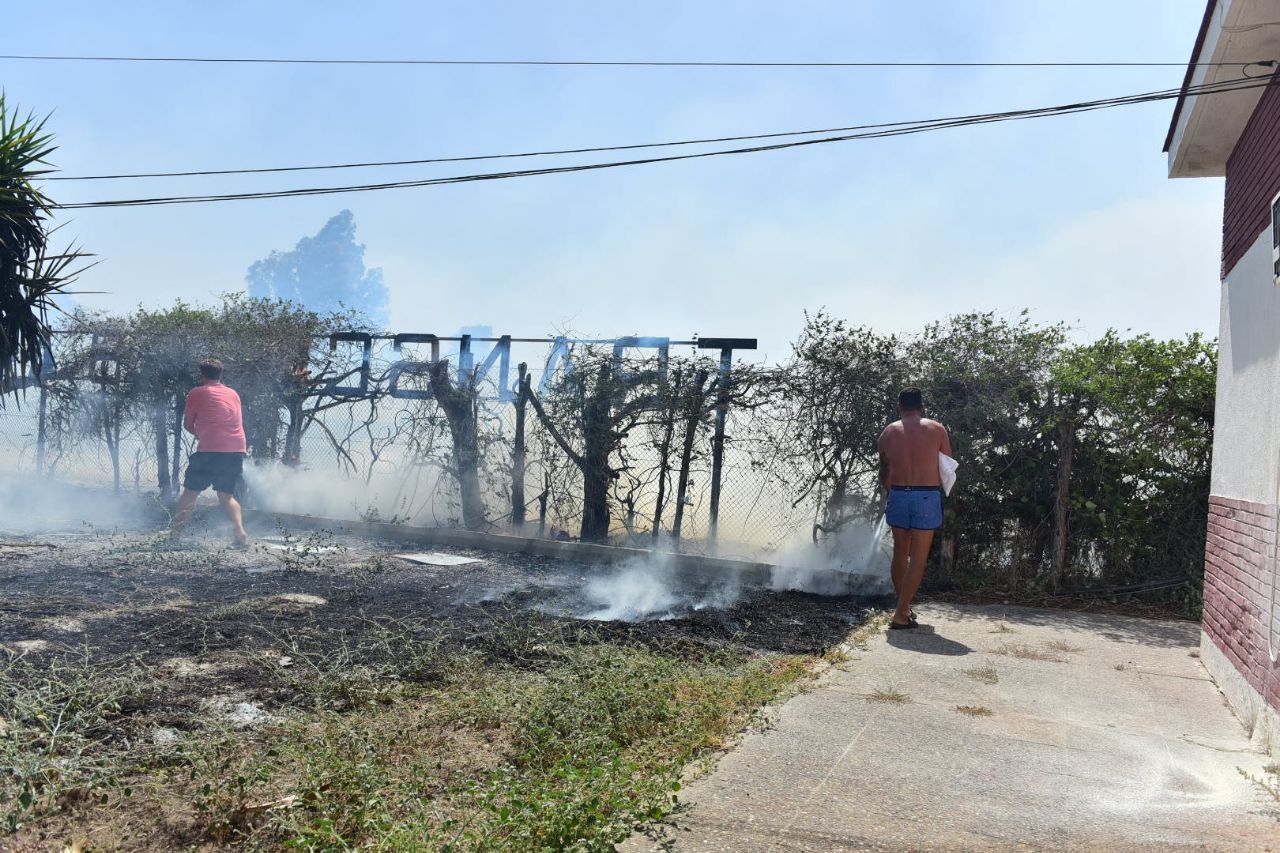 Dos hombres tratan de sofocar las llamas, alcanzando ya la cochera de la empresa Transcela en Puerto Real, en la tarde de este domingo.