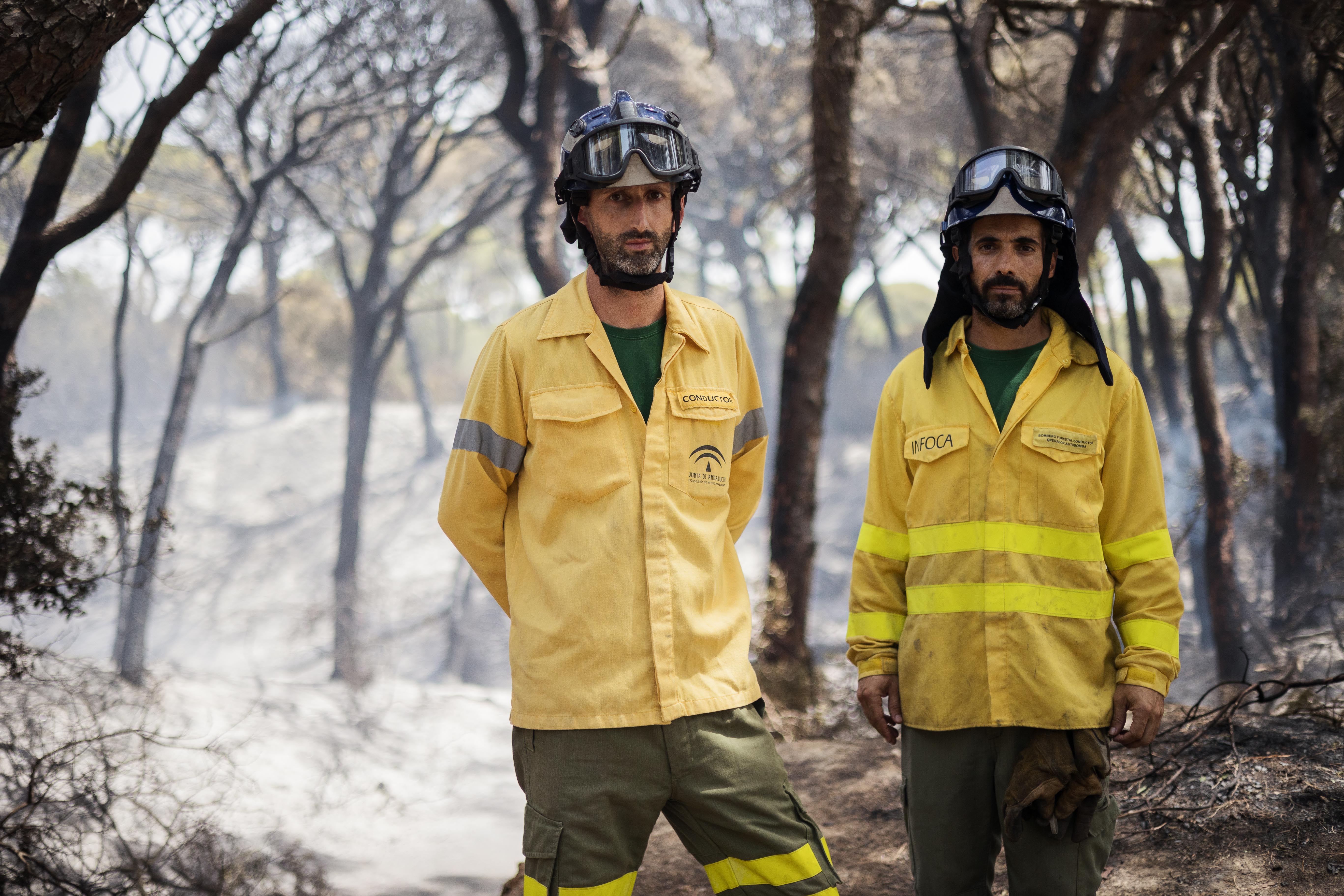 Dos bomberos del Plan Infoca posan para lavozdelsur.es con Las Canteras de fondo.