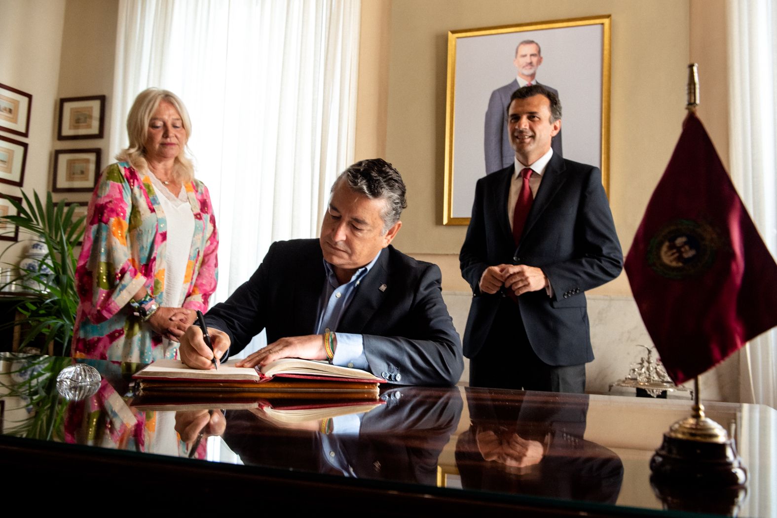 Sanz firma en el libro de honor de la Alcaldía ante la delegada de la Junta, Mercedes Colombo, y el alcalde.