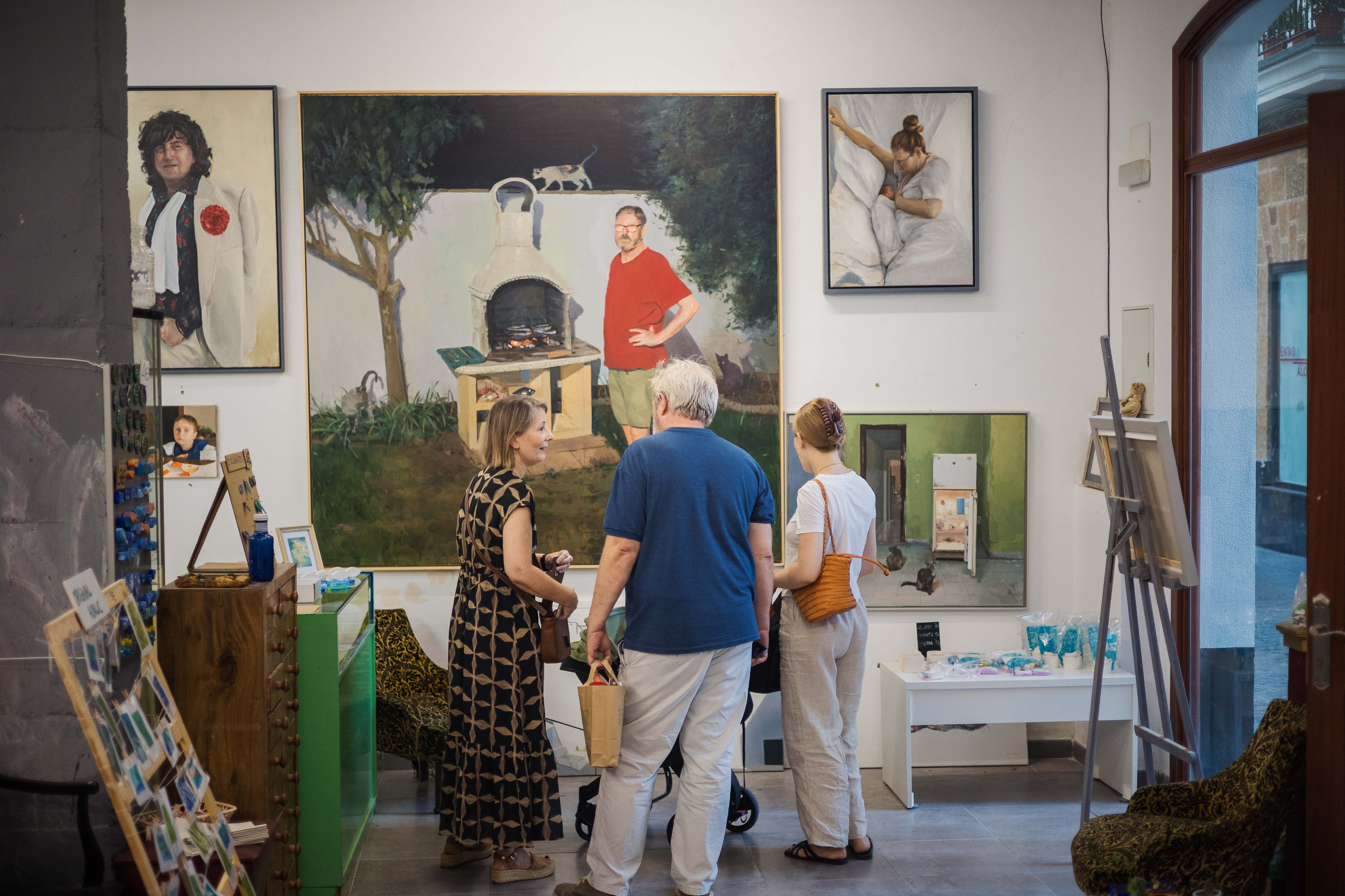 Visitantes en la galería-estudio de Pepe Baena contemplando la obra de su padre cocinando en una barbacoa.