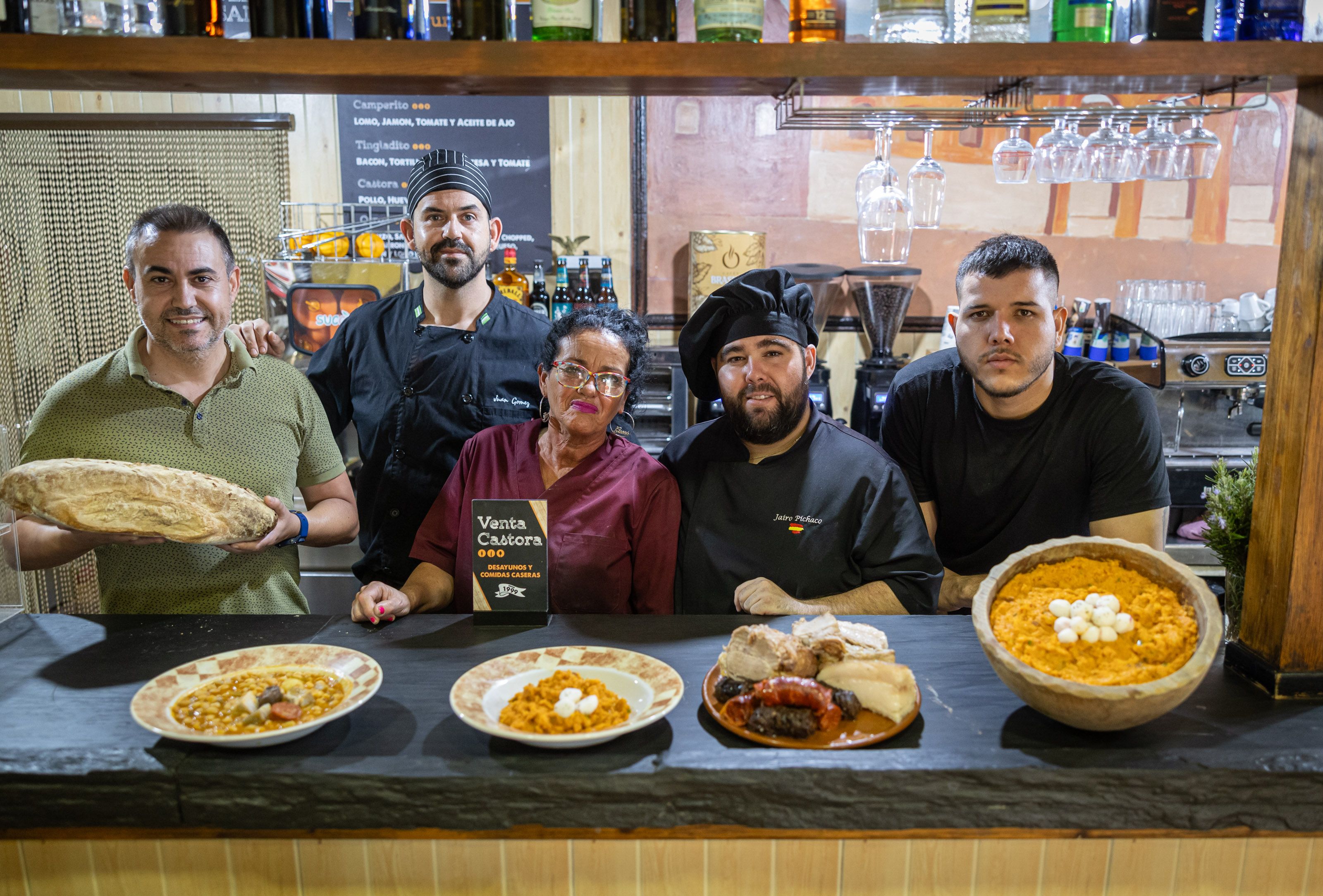 En el extremo izquierdo en la imagen, Israel Caro, junto al personal de cocina y sala de Venta Castora, y los platos estrellas de la cocina de toda la vida del negocio de El Portal, en Jerez.