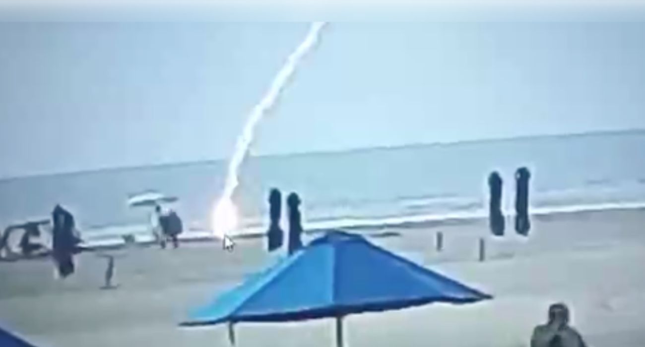 Momento en el que un rayo alcanza a una mujer en una playa.
