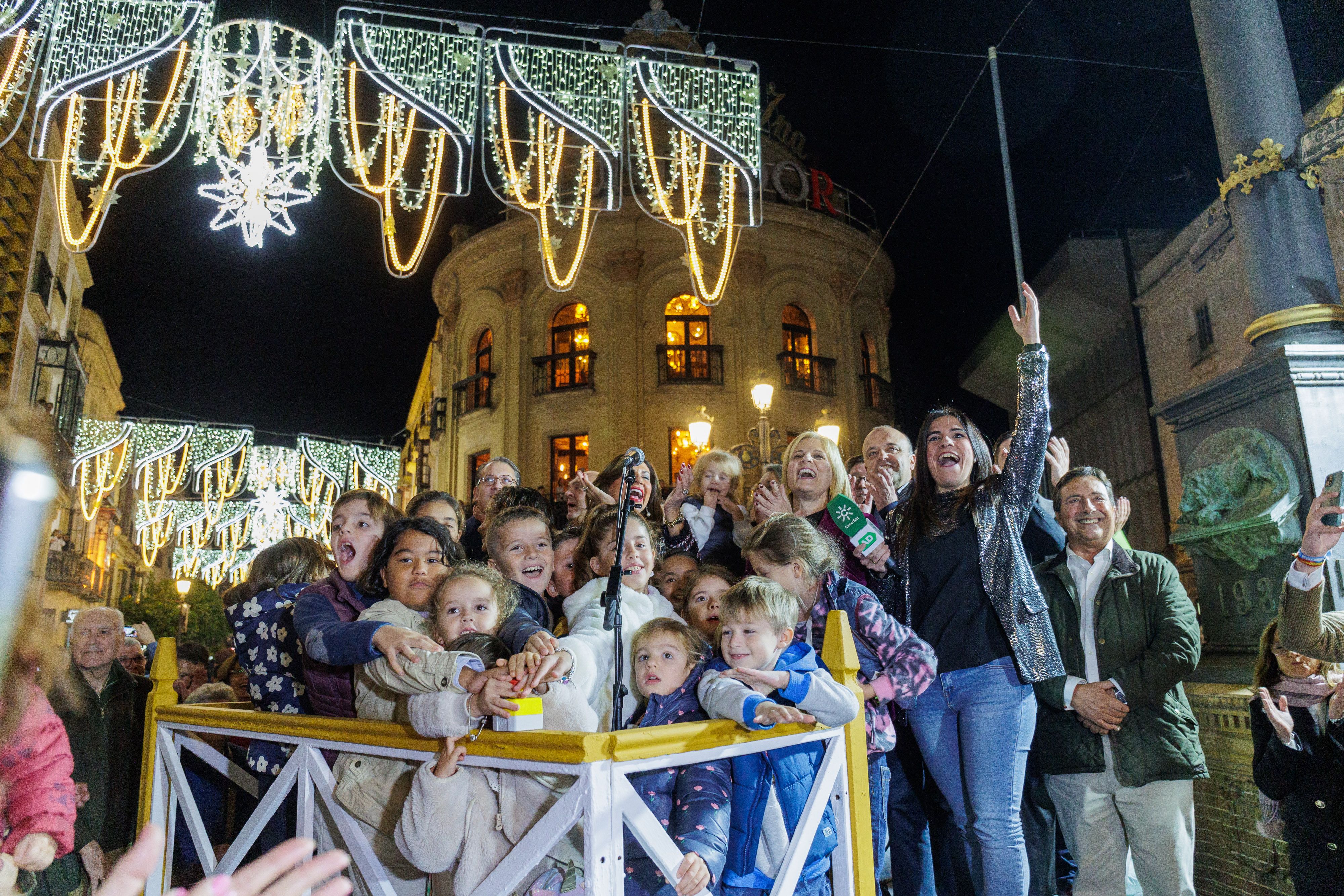 Encendido del alumbrado de Navidad en Jerez, en una imagen con niños y responsables municipales, con la alcaldesa Pelayo al frente, y una reportera de Canal Sur.