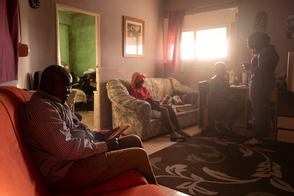 Moisés, leyendo en el sofá de su casa, con algunos de sus hijos al fondo. FOTO: MANU GARCÍA