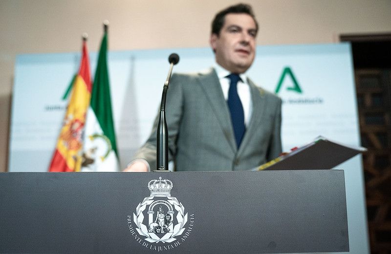 El presidente andaluz, Juan Manuel Moreno, en un atril con el símbolo oficial de Andalucía modificado.