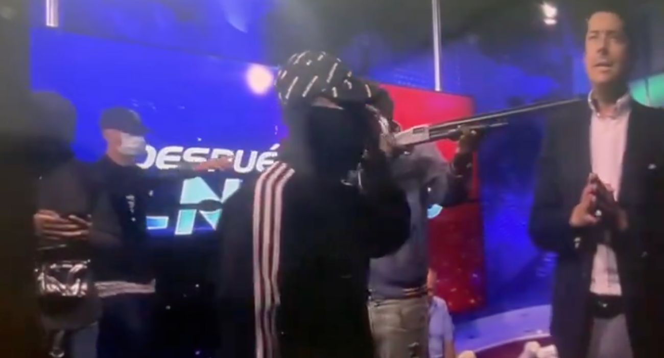 Uno de los encapuchados, encañonando al presentador del programa de televisión.