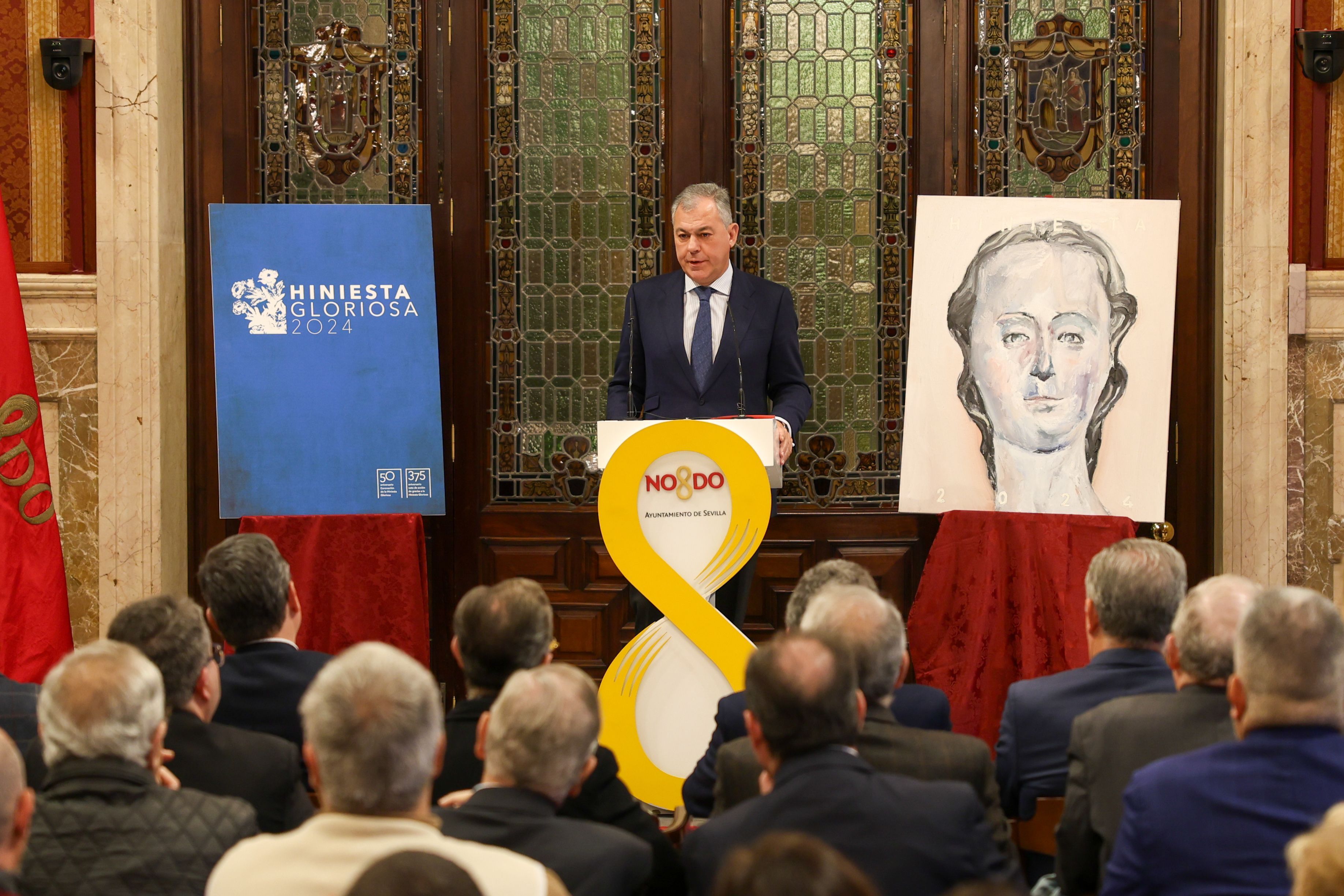 El alcalde de Sevilla durante su intervención en el acto, entre el cartel y el logotipo. 