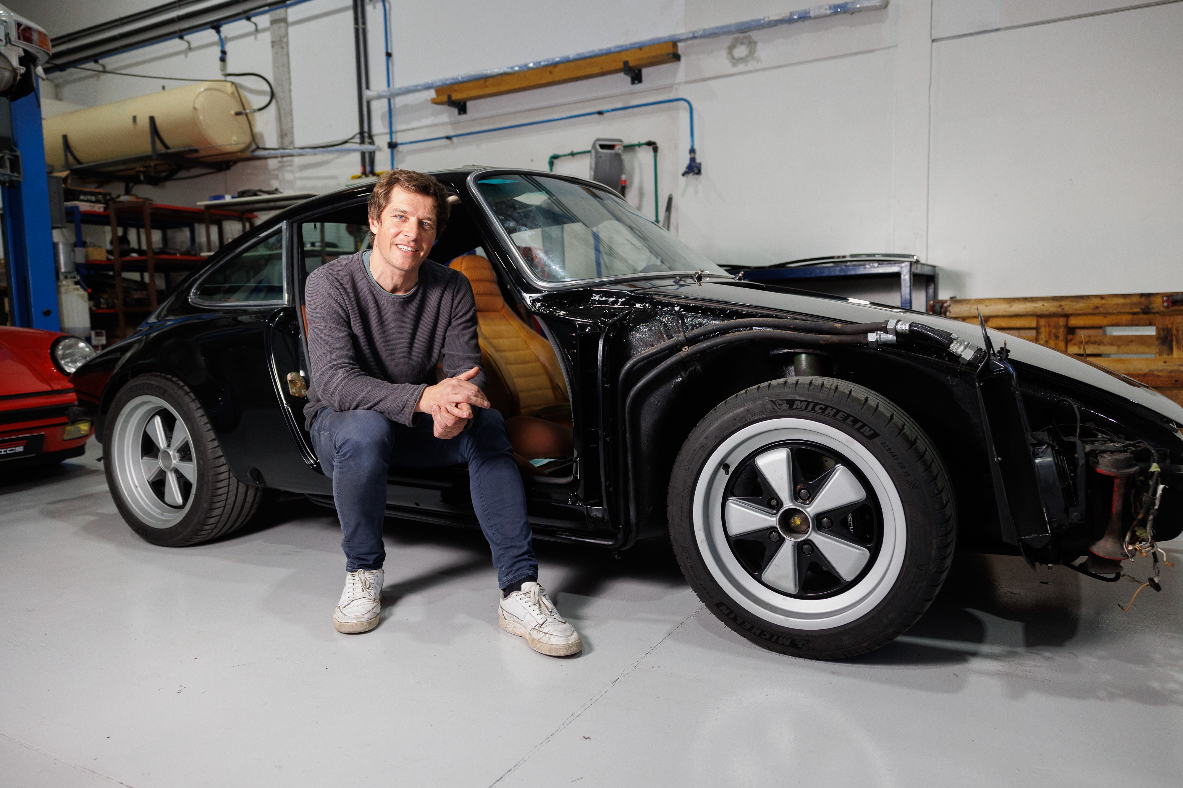 El francés posa junto a un coche restaurado en el taller.