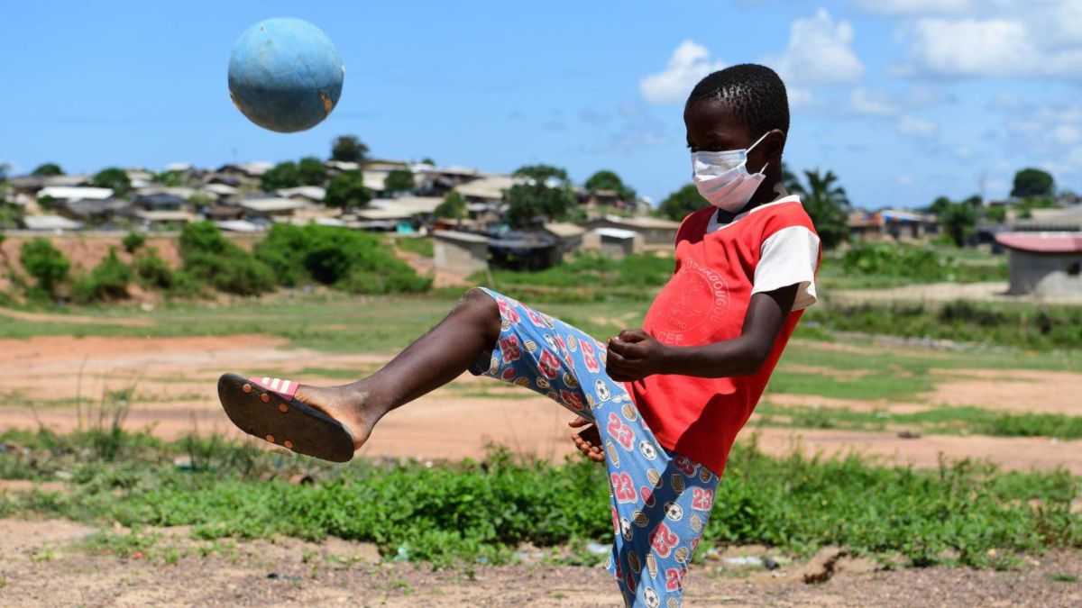 Un niño de ascendencia africana juega al fútbol con mascarilla. FOTO: Unicef