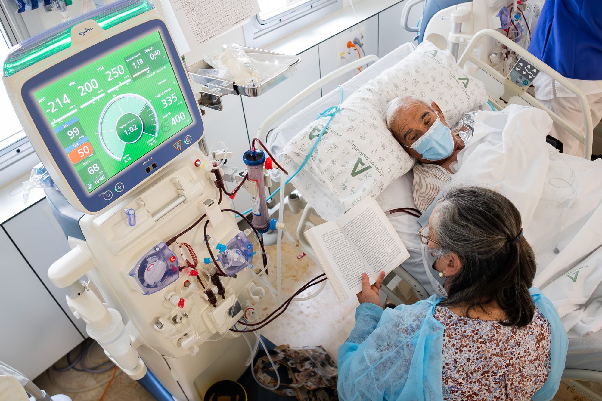 Mercedes, voluntaria del proyecto 'Medicina para el alma', lee en voz alta a Pedro durante su sesión de hemodiálisis.