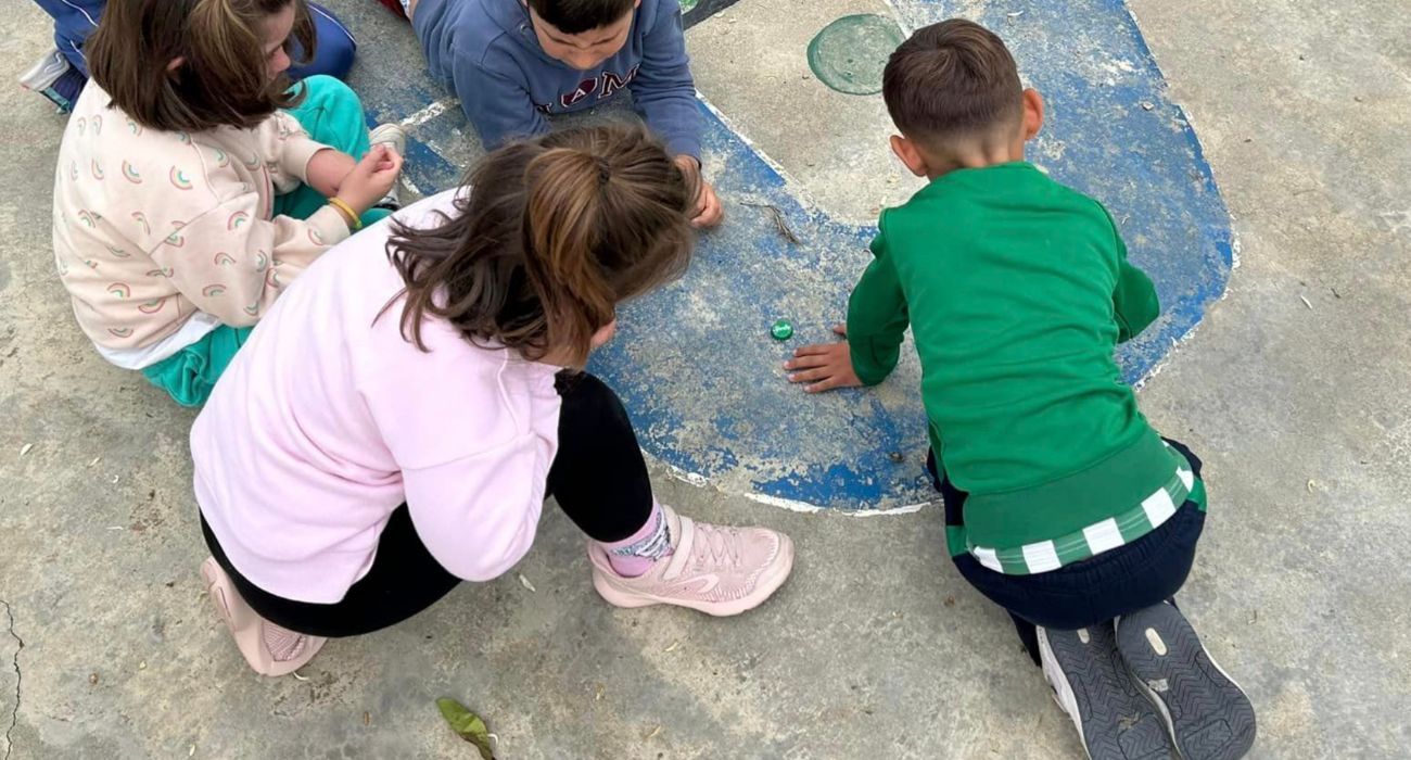 Varias niñas y niños juegan a las chapas en el patio de un colegio.