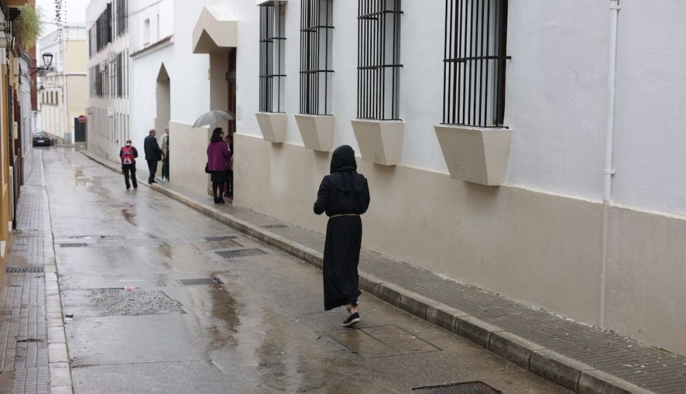 Un solitario nazareno de Amor Sacrificio por una calle mojada por la lluvia. 