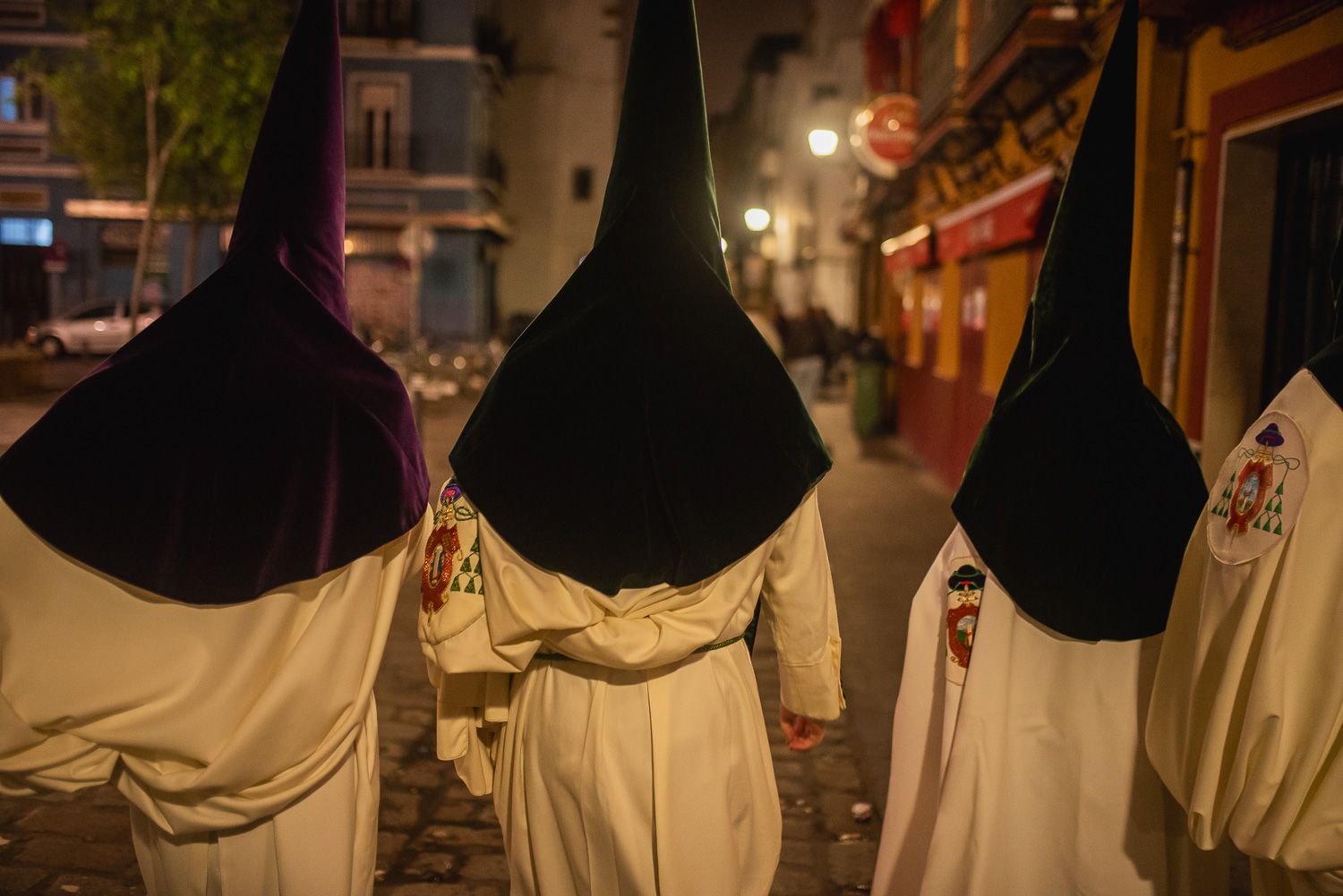 Tres nazarenos de la Madrugá pasando por delante de un bar cerrado.