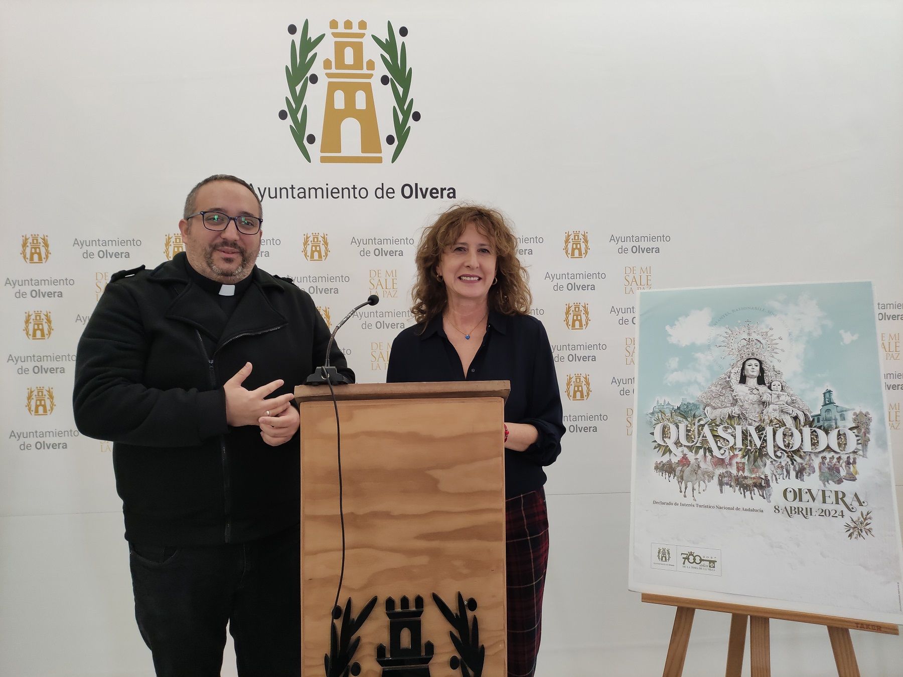 Una romería con 300 años de tradición en Olvera: el Lunes de Quasimodo. La alcaldesa y el párroco de Olvera junto al cartel de las fiestas. 