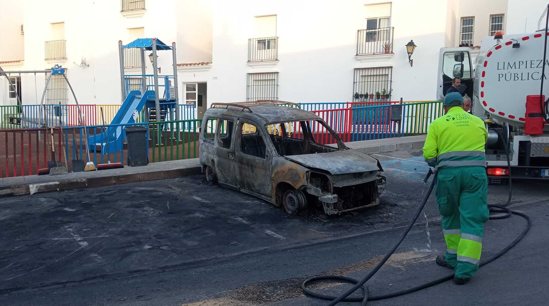 Un operario riega la zona donde han ardido varios coches en Vejer.