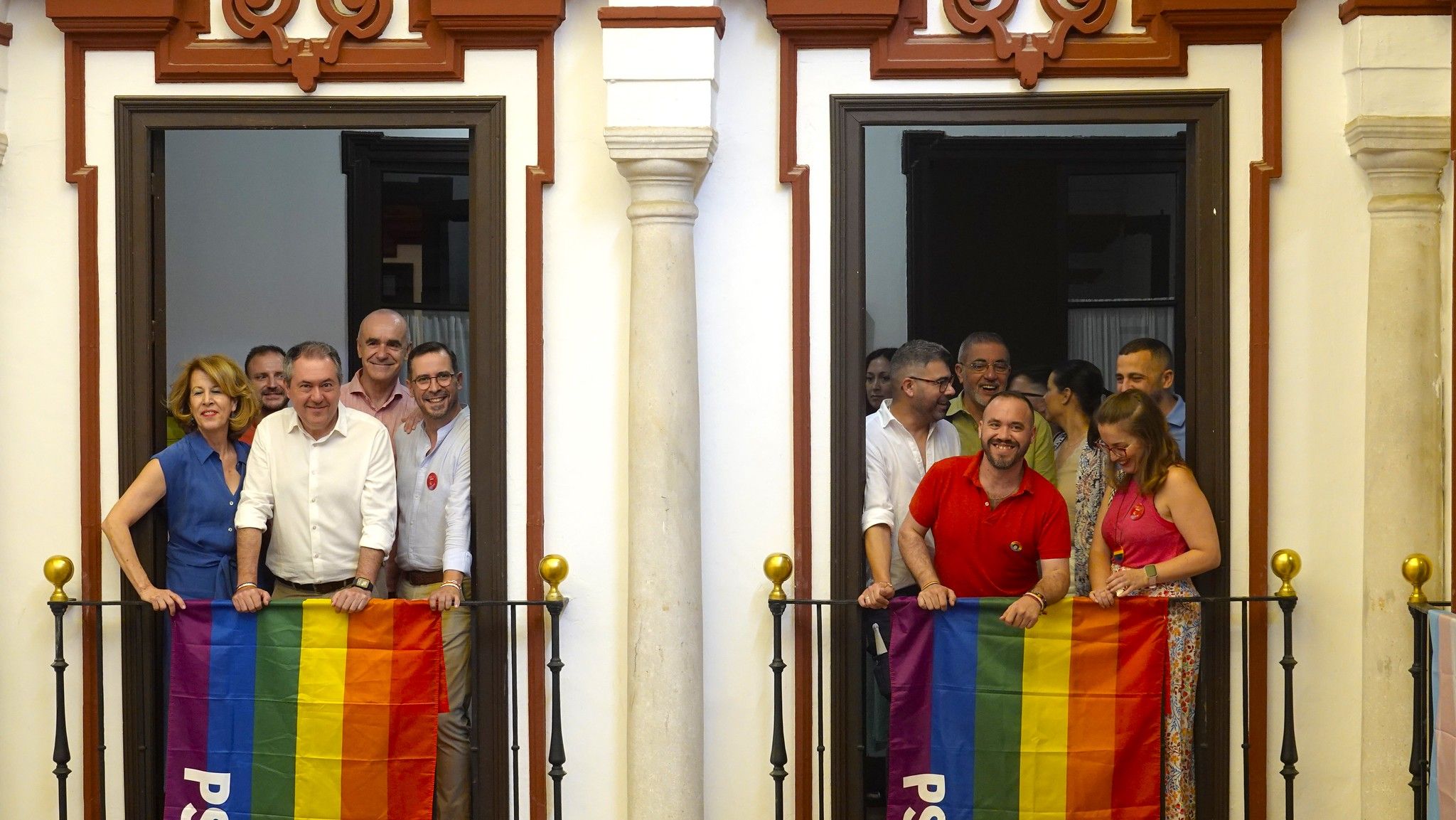 El secretario LGTBI, Manuel Rosado, de rojo, en uno de los balcones de la sede del PSOE, junto a Juan Espadas.