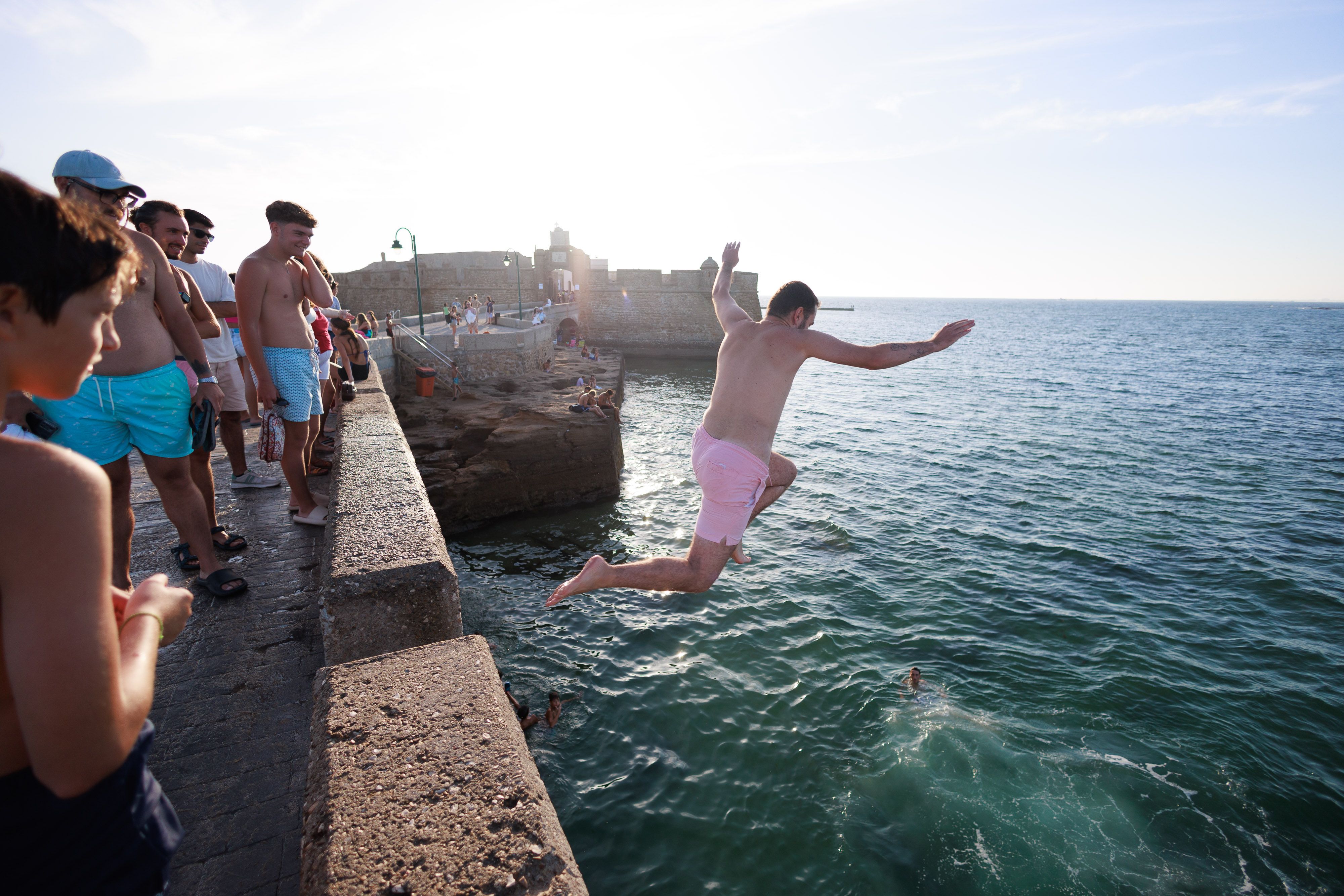 Un hombre se tira al agua en el día de reapertura del Castillo de San Sebastián de Cádiz, al fondo de la fotografía.
