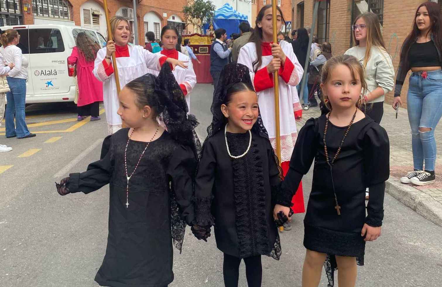 Tres pequeñas vestidas de mantilla, con el paso al fondo.