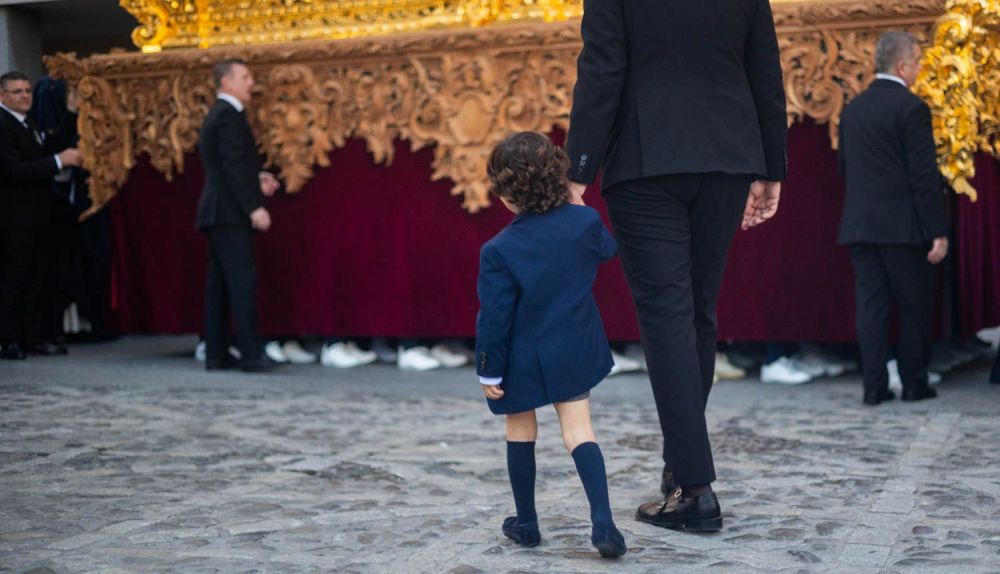 Un niño cogido de la mano de uno de los capataces viendo los pies de los costaleros