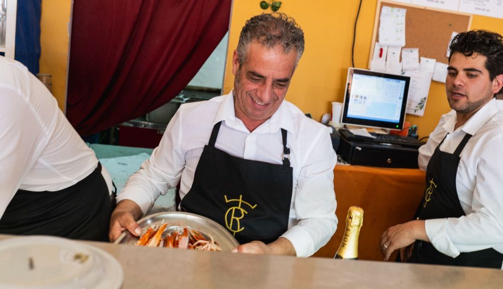 Sonriendo, al otro lado de la barra.  