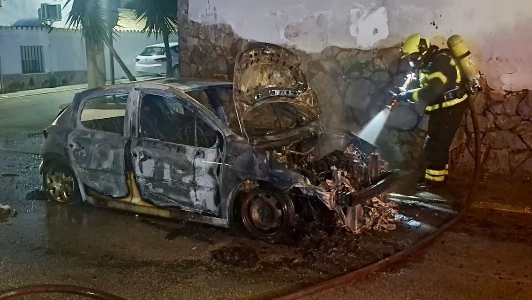 Bomberos apagando las llamas del coche calcinado en Torrecera.